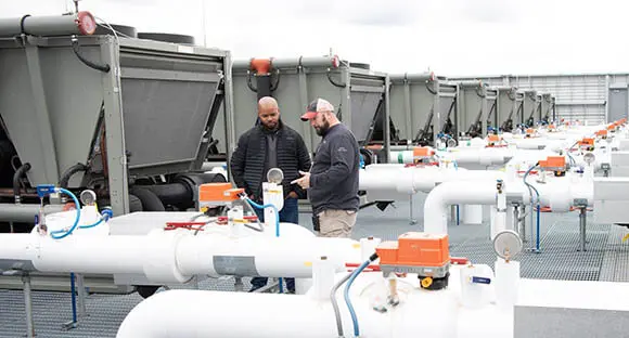 two men on roof looking at pipes